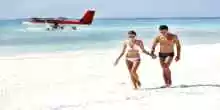 Attractive young couple walking on the beach with a seplane floating in the background