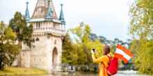 Young female traveler with austrian flag taking picture in front of Franzensburg castle in Laxenburg town. Traveling in Austria